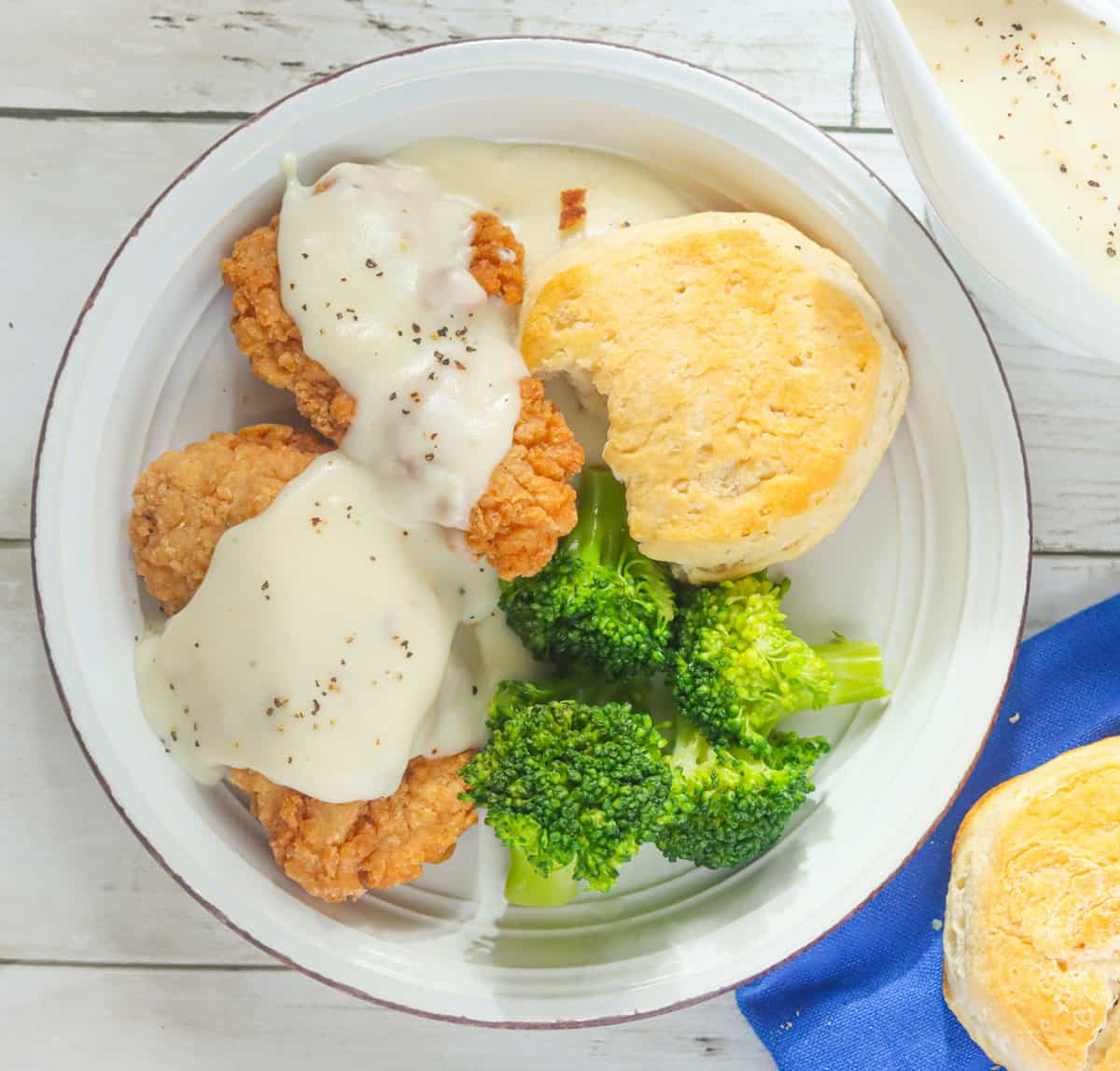 White gravy over chicken steak, biscuits, and broccoli